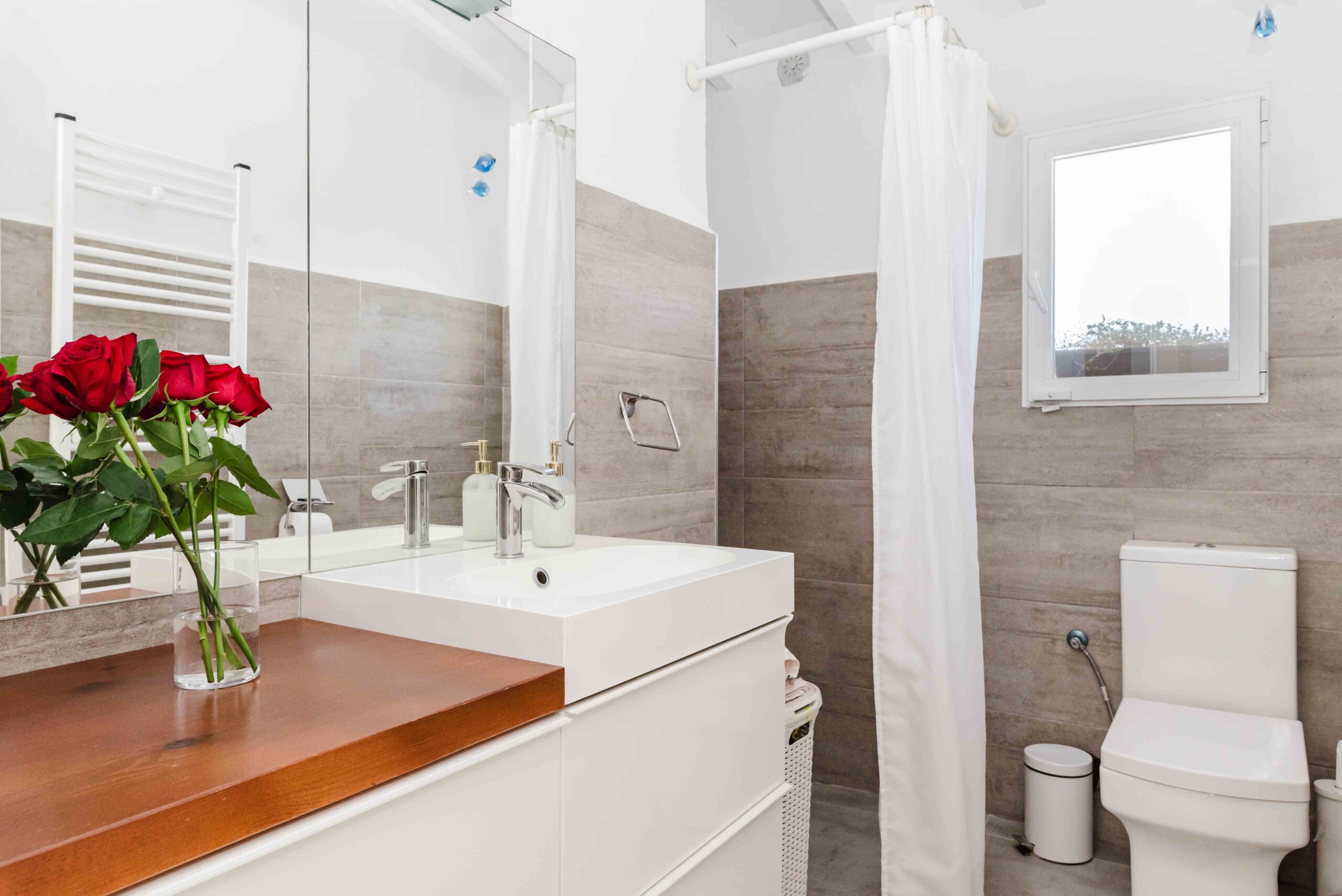 Baño en suite luminoso con lavabo, ducha y detalles decorativos en tonos claros